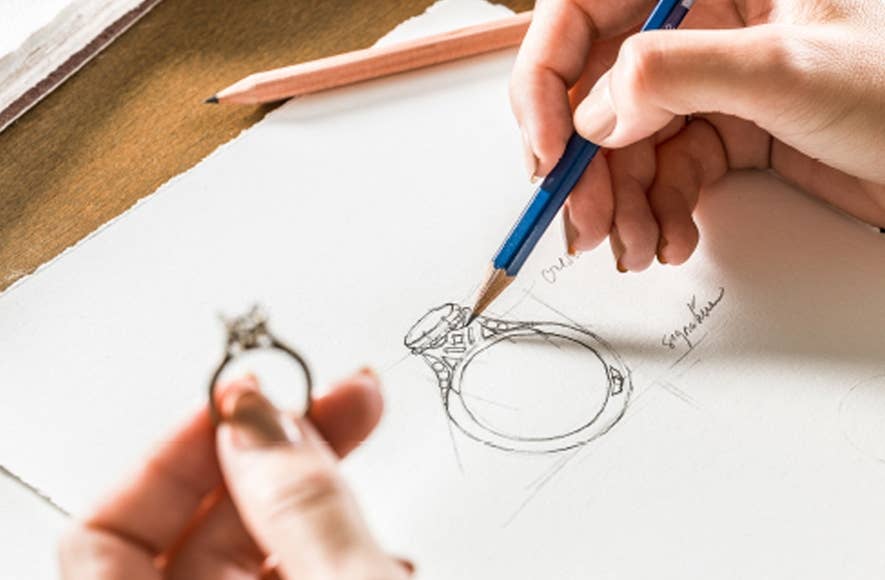 Left hand holding engagement ring and right hand sketching the design