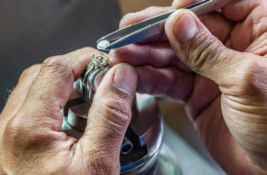 Close up of two hands setting a diamond into a TACORI design engagement ring